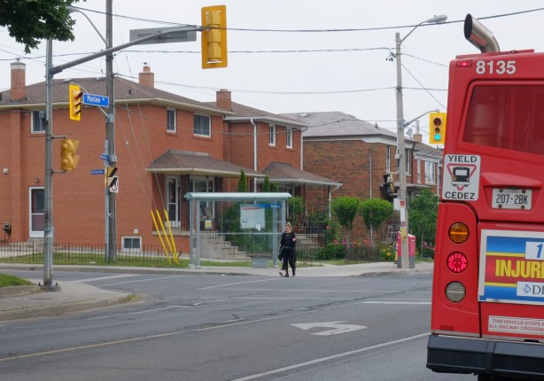 the back of a TTC bus on Marlee Ave by Ridelle Ave stop, a woman crosses the road, two storey brick houses