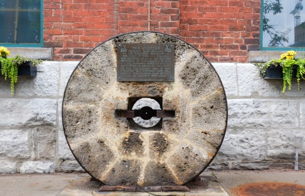 large stone, round with hole in middle, plaque attached, old millstone from the distillery, made in 1832