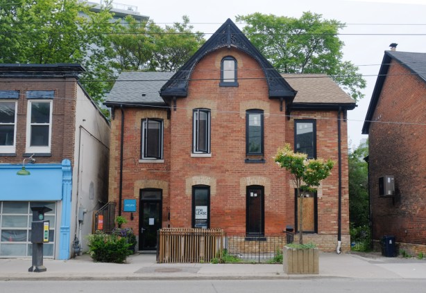 old brick semi detached house, red brick, with black roof, central peak, on Queen East, heritage property
