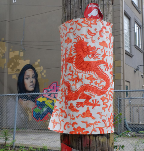 an intricate painting of an orange dragon on whitepaper, stapled to pole in graffiti alley, with portrait of a woman in the background
