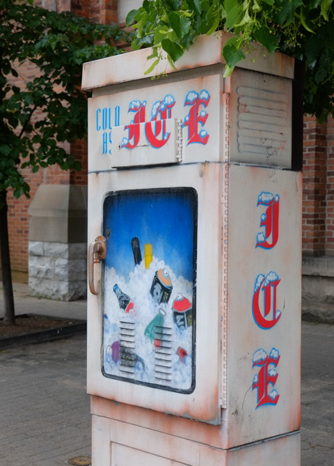 sidewalk metal box that has been painted to look like a box that dispenses or sells ice 