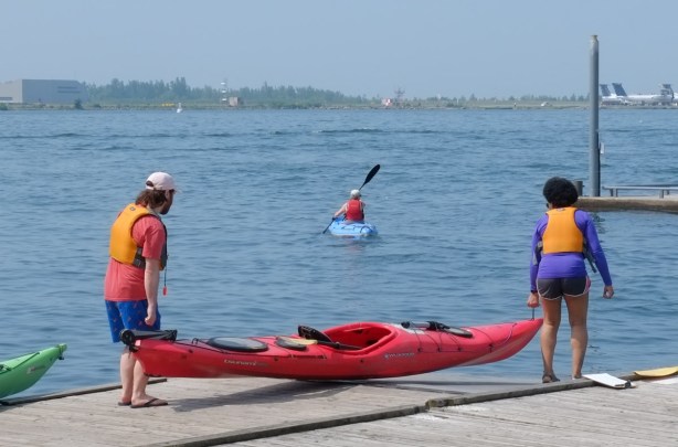 two people putting a red kayak in the water while a third person is in a blue kayak already on the water 