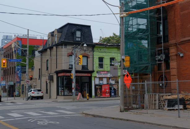 looking south on Sumach, west side, from Queen, renovations at Dominion pub on the right, two older buildings on the south side, one with black mansard roof, and the other painted bright green