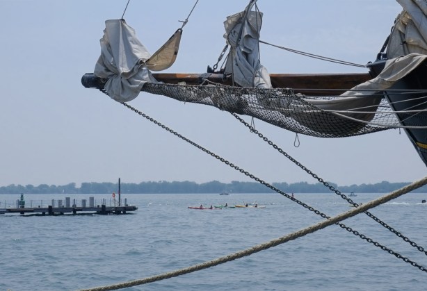 rigging, ropes and chains from a boat in the foreground, kayaks on the water in the distance