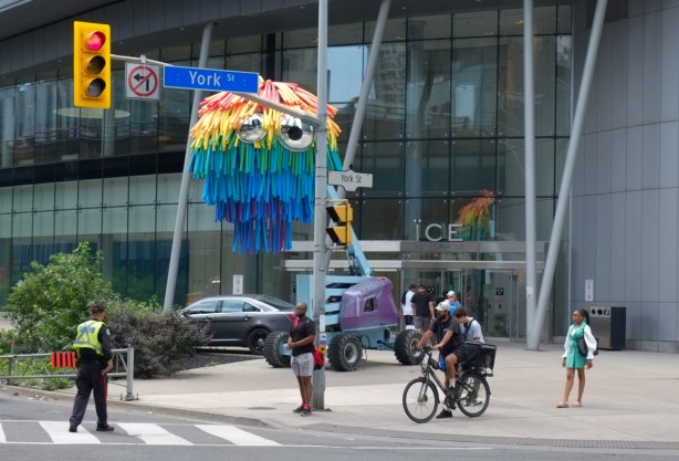 shaggy rainbow coloured mop-like structure over a boom, raised about 20 feet off the ground, with googly eyes, boom town art installation