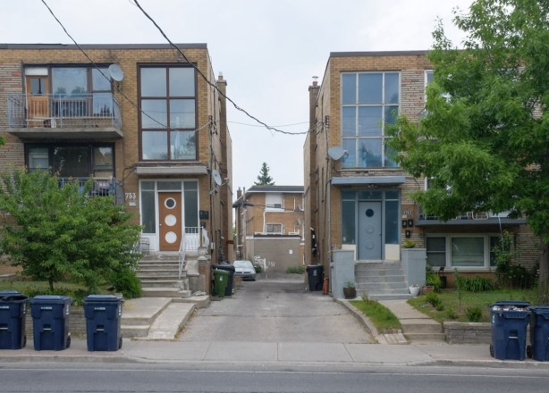 looking down a driveway between two small apartment buildings to the back of another residential building