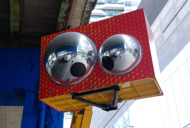 on a construction boom, painted red, two big half globes, reflective, with googly eyes, also underneath, a black triangle that looks like a smiling mouth