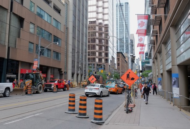 street scene, Queen St. East downtown Toronto, construction, Canadian flags ,pedestrians, tall buildings, 