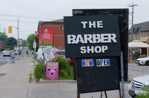 sign saying that the barber shop is now open, black sign, beside sidewalk