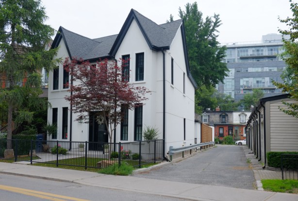 two white houses with black trim, semi, with an alley beside, looking down the alley to row houses on another street