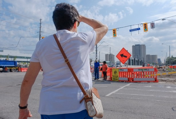 a woman in white looks to the other side of the street as she waits for traffic light to turn green, a couple wait on the other side