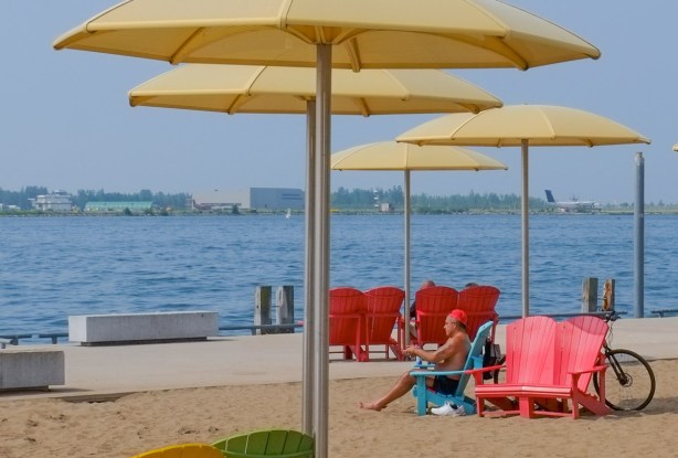 man sitting in red muskoka chair under yellow umbrella, toronto waterfront, sand