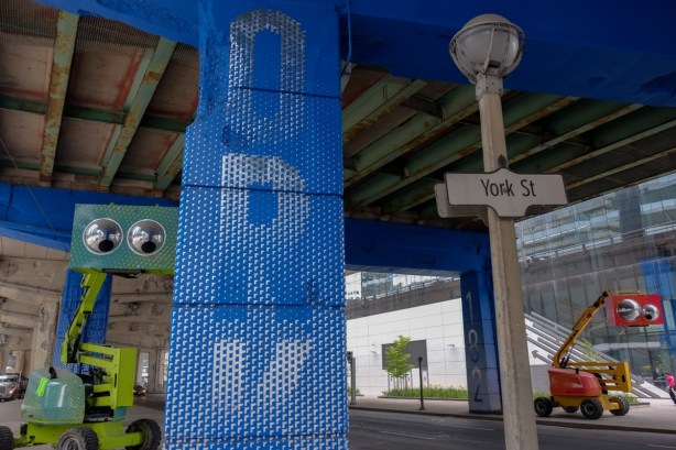 two booms, one green, one red, with eyes, parked under the Gardiner, by bents that have been decorated in blue 