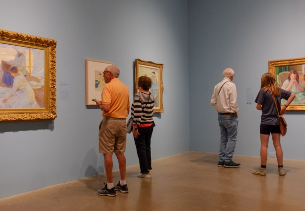 people looking at paintings on a wall in an art gallery