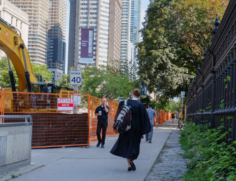 a woman in black robes walks up the sidewalk on University ave