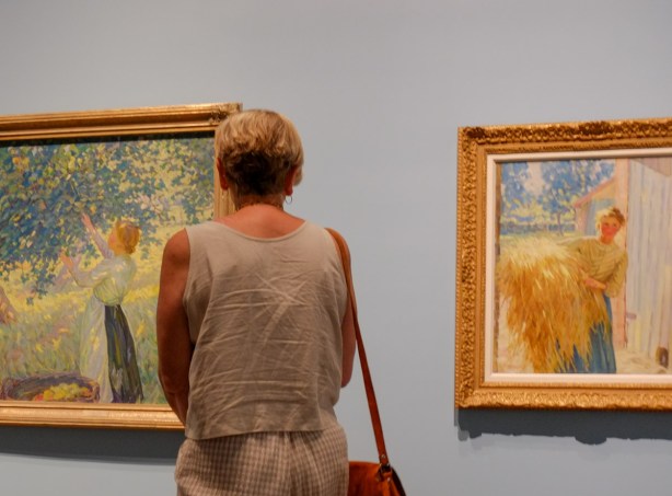 woman looking at two impressionist paintings, back to camera