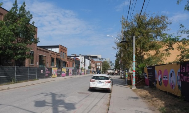 looking north on Atlantic Avenue from the south end, a white car parked there, many buildings now empty with hoardings in front for metrolinx onstruction