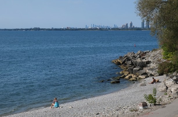 two people sitting on the beah at ontario place, lake ontario, mississauga and western GTA in the background
