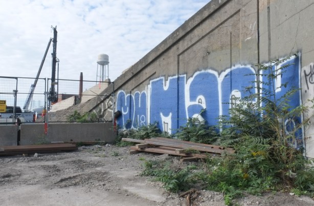 text graffiti in blue and white on the side of a railway bridge, water tower in the background