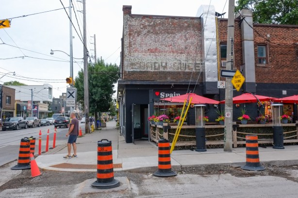 ghost coca cola sign on side of old store, now a Spanish restaurant, with red umbrellas on patio