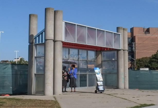 two women with an umbrella on a sunny day, under a concrete and glass structure