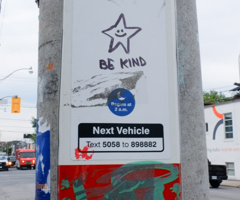 on a TTC bus stop sign, a black marker drawing of a star with a happy face in the middle of it, with the words be kind