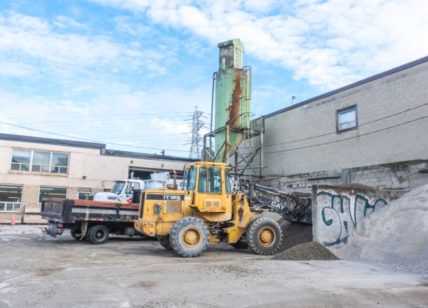 yellow front end loader in front of building, large green storage tank behind