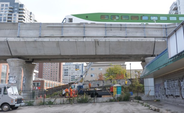 green and white GO train passes over new elevated section of tracks as it crosses Dupont Ave