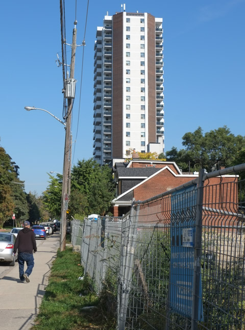 man walking past construction site with tall condo tower as well as single family houses in the background
