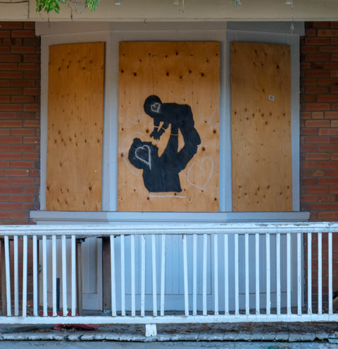 two black silhouettes painted on plywood covering a window, parent holding up young child in air above head