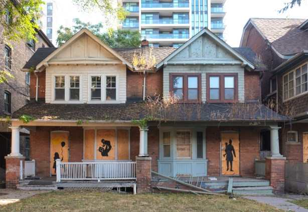 black silhouettes of people painted on plywood used to board up doors and windows of two empty houses waiting to be demolished