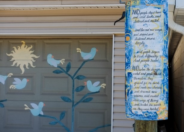 hand written poem story on board, hanging next to a garage with paintings of birds in a tree