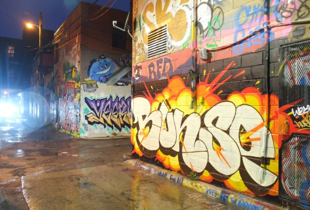 Graffiti Alley night time, light from headlights of car, walls covered with street art and graffiti