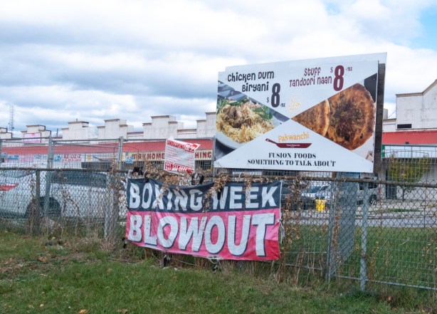 old banners on a chainlink fence advertising boxing week specials, ads for restaurant food,