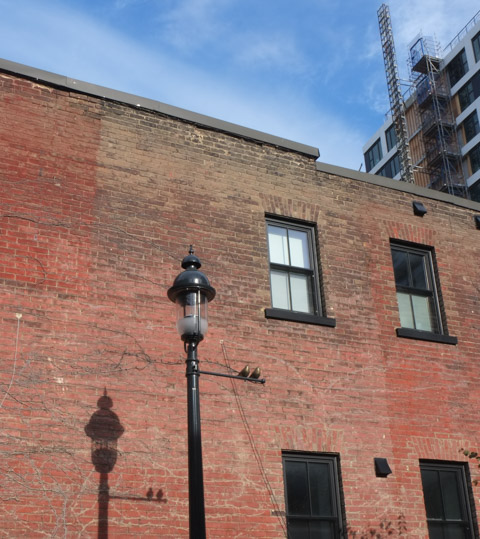 shadow of old light pole on brick wall of house, new condo being built behind, draper street