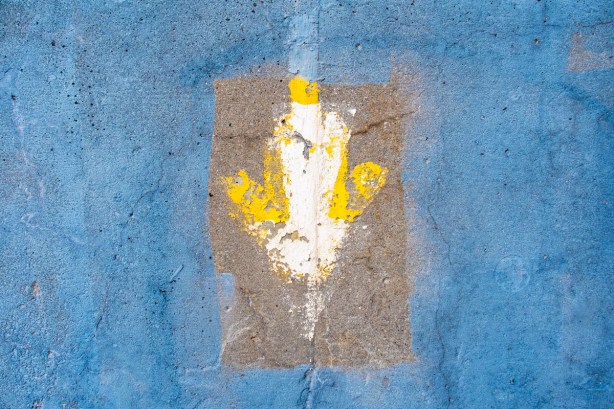 downward arrow shape painted in yellow and white on blue concrete under a brdge
