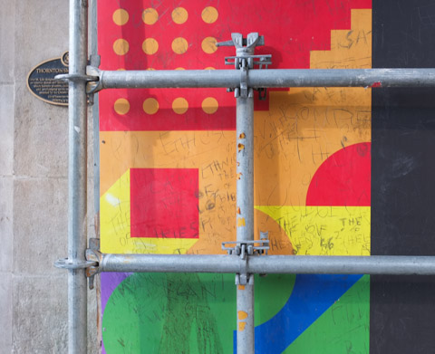 ink and marker scrawls on coloured hoardings around construction site 