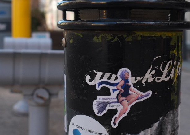 graffiti sticker on a black pole, woman riding a broomstick