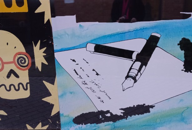part of a larger mural, fountain pen lying on white piece of paper, words written, ink blots on paper and table