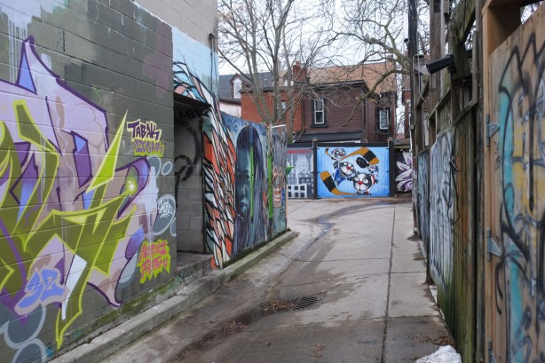 murals on garages at the end of the lane with other murals on the buildings on the side of the alley too