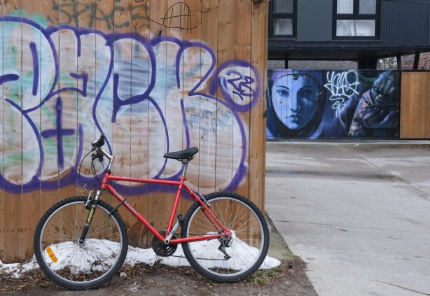 a bike leaning against a wall in an alley, a street art mural of a woman in blue paint in the background