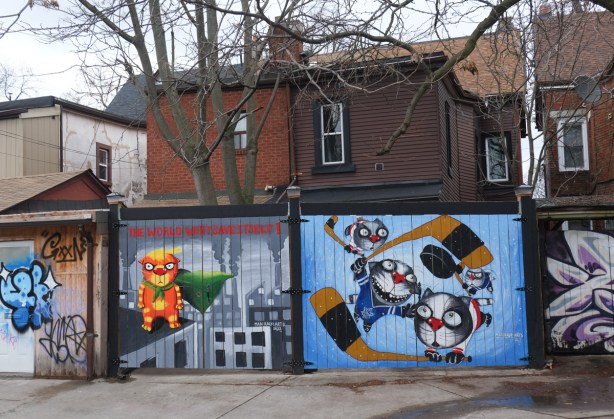 murals on garages, one of the right is cats playing hockey and on the left is a cat with text saying 