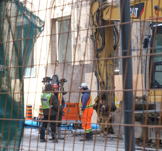 looking through metal construction fence, workmen on a construction site talking to each other