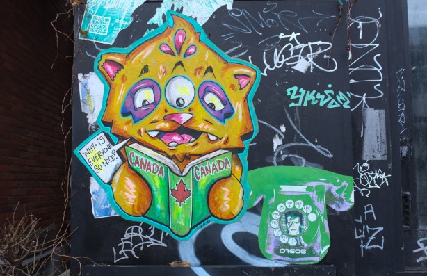 NYC based artist City Kitty cat reading a book about Canada and saying Canada why are you so nice beside a second pasteup of a rotary phone with David Bowie's face in the middle of it 