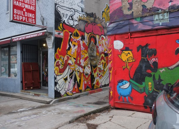 part of an uber 5000 mural of dogs playing cards, with a little yellow birdie in the top left corner, entrance to alley, other graffiti and street art can be seen including a large piece by Rowell Soller