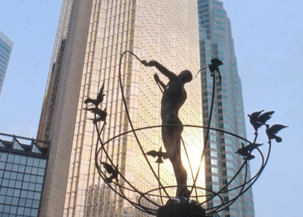 sculpture outside union station, man with birds flying around him in partial sphere shape, gold coloured rbc building behind him