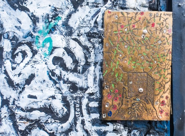 engraved and coloured brass rectangle street art, beside part of a black and white mural