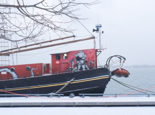 picture of an octopus painted on the side of a red and black boat that is tied up at the shore