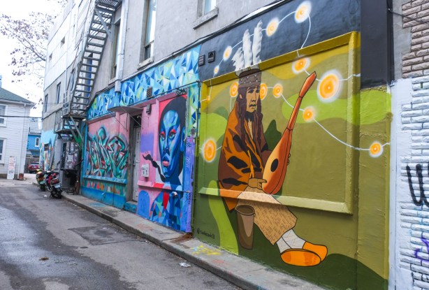 murals in a kensington alley, in the front is a mandolin olayer, then a portrait in blue.