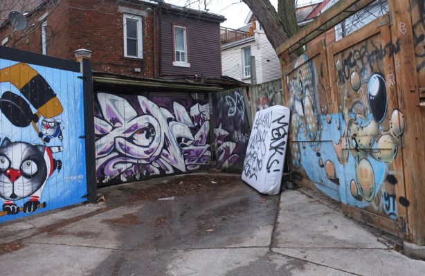 an old mattress leaning against a fence in an alley, murals on some of the garages, 